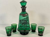 Green glass decanter with silver overlay and stopper, shown with four matching small green glasses arranged around it on a white background.