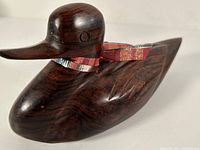 Front and top angled view showing the duck's smooth wood surface, carved wings, circular eye detail, and decorative ribbon tied around the neck.