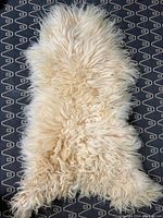 Natural cream-colored sheep skin rug with long curly wool fibers, shown from front side displaying fluffy texture and natural edges.
