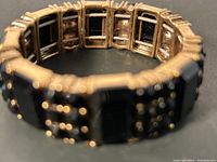 Close-up photo showing the linked brass tone segments and black square insets of the bracelet, highlighting the elastic band construction and surface details.