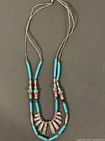 Full view of the necklace showing its double strand design with turquoise beads, silver-tone accents, and multicolor stones on a black background.