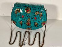 Front view of vintage purse showing turquoise mosaic tiles, gold floral designs, red stones, and chain strap.