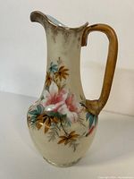Photo of the full ceramic pitcher with curved spout, brown handle, and hand painted floral design.
