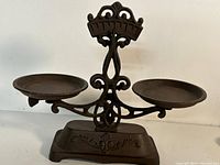 Front view of the old cast iron balance scale with two round pans and decorative detailing on the frame and base.