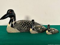 Front-side view of three wooden loon decoys arranged by descending size on a green surface showing detailed paint and craftsmanship.