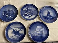 Overview photo showing all five Copenhagen collector plates arranged on a cloth, blue and white, each with a unique design and year marking.