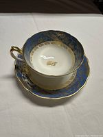 Front angle view of the Paragon teacup inside the matching saucer showing blue and gold decorative pattern and scalloped edges.