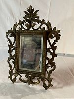Front view of heavy ornate brass frame with mirror showing intricate leaf and scrollwork design, warm patina.