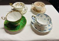 Four teacups with matching saucers arranged together, showing different designs and colors.