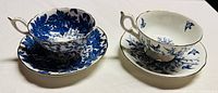 Two pairs of Coalport teacups and saucers displayed side by side showing blue floral patterns with gold trim on white porcelain.
