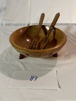 Wooden bowl containing a wooden fork and spoon on a white surface, showcasing the bowl's shape and the utensils.