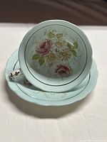 Teacup and saucer stacked showing the painted floral design inside the cup and on the saucer with aqua background.