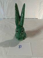 Front view of green ceramic bunny figurine with long upright ears showing texture and painted eyes.