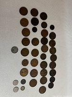 Top-down view of 38 British coins laid out on white fabric background comprising various sizes and metals including bronze and silver coins dating from 1866 to Queen Elizabeth.