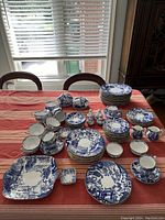 Overview of entire set laid out on table under window, showing stacks of plates, cups, saucers, shakers and platters.