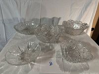 Five intricately cut glass bowls displayed on a white backdrop, showing variety in shape and size, all clear glass with complex cut patterns.
