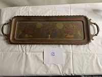 Full view of the rectangular brass tray with front and back handles, lying on white fabric showing minor surface wear.