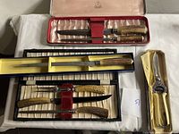 Top-down view of the set containing 3 knives and 1 fork with stag horn handles, housed in three different fitted cases with satin linings in red, yellow, and black.