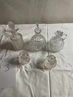 Overview of all five glass condiment containers arranged on a white cloth background showing variety in size and style.