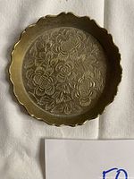 Top-down image of the small Indian brass plate showing floral engravings and scalloped edge.
