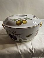 Side view of the covered porcelain casserole dish showing hand-painted fruit design and gold handles
