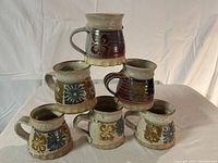 Photo showing six stoneware mugs stacked and arranged to display their colors and designs.