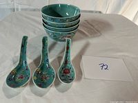 Set of five robin's egg blue ceramic Chinese bowls stacked with five matching ceramic spoons lying in front, showing hand-painted floral designs.