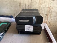 Side and front view of two black Xbox 360 consoles stacked, showing front features and wear