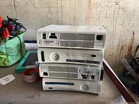 Four white Xbox 360 consoles stacked, showing the front and top sides, with visible disc drives and power buttons.