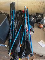 Photo showing five pairs (10 total) hiking poles in blue and black with wrist straps, some branded, along with their black carrying bags on a surface with other items.