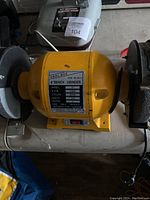 Photo of yellow 6-inch bench grinder with label showing specifications and power switch.