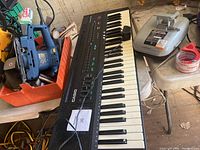 Casio keyboard piano showing 61 keys and control buttons in black. Includes some surrounding items but keyboard is main focus.