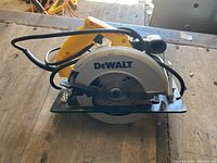 Front view of yellow and black DeWALT circular saw on wooden surface showing the blade guard, handle, and power cord.