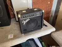 Photo of a black Fender guitar amplifier with control panel and handle, resting on a table.