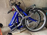 Folded blue CCM Roadmaster bicycle showing frame, rear carrier, handlebars, and tires in compact storage position.