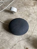 Photo of charcoal Google Nest Mini smart speaker and white power adapter on wooden surface.