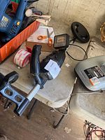Photo showing the RadioShack metal detector on a table surrounded by various tools and items, highlighting the control panel, handle, and circular search coil.