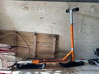 Full side profile of the orange Stiga Snow Kick scooter showing snow skis, frame, and platform.