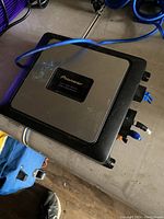 View of the amplifier showing silver plate with Pioneer logo, connected cables and black plastic edges, placed on a wooden surface.