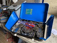 Blue portable propane camp stove open showing two burners and metal wind guards.
