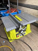 Ryobi 15 amp table saw with metal table surface, adjustable fence, power switch, and height adjustment dial visible.