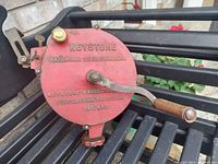 Close-up of red cast iron grinder housing with brass oil cap and wooden crank handle showing brand and model info.