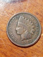 Obverse side of the 1902 US Indian Head Penny showing Lady Liberty in a feathered headdress and the date 1902, the coin shows wear and a brown patina.