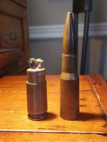 Front view of WW1 bullet lighter with lighter mechanism exposed, standing upright on wooden surface.