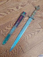 Full view of dagger and sheath on wood floor showing decorative tri-metal handle and sheath colors