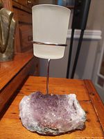 Amethyst geode tealight holder standing on wooden surface, showing frosted glass tealight holder held by slim metal stand attached to amethyst crystal base.