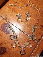 Necklace and earrings arranged on a wood surface, showing clear faceted teardrop pendants in light golden and blue tones and smaller round beads.