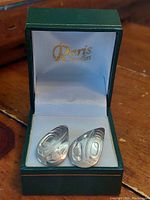 Pair of silver teardrop-shaped earrings with First Nations engravings displayed inside a green Paris Jewellers box.