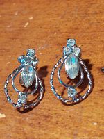 Pair of vintage sterling silver screw clamp earrings on a wooden surface showing twisted metal loops, central marquise semi-precious stones, and round clear stones.