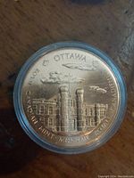 Obverse side of bronze medal showing design of the Ottawa Royal Canadian Mint building, with Latin lettering around the edge.
